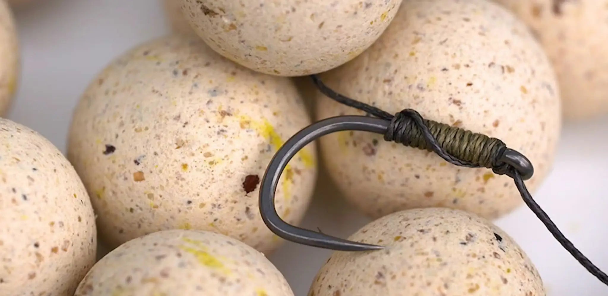 Dark metallic fishing hook with greenish-brown thread knot for wafter rig