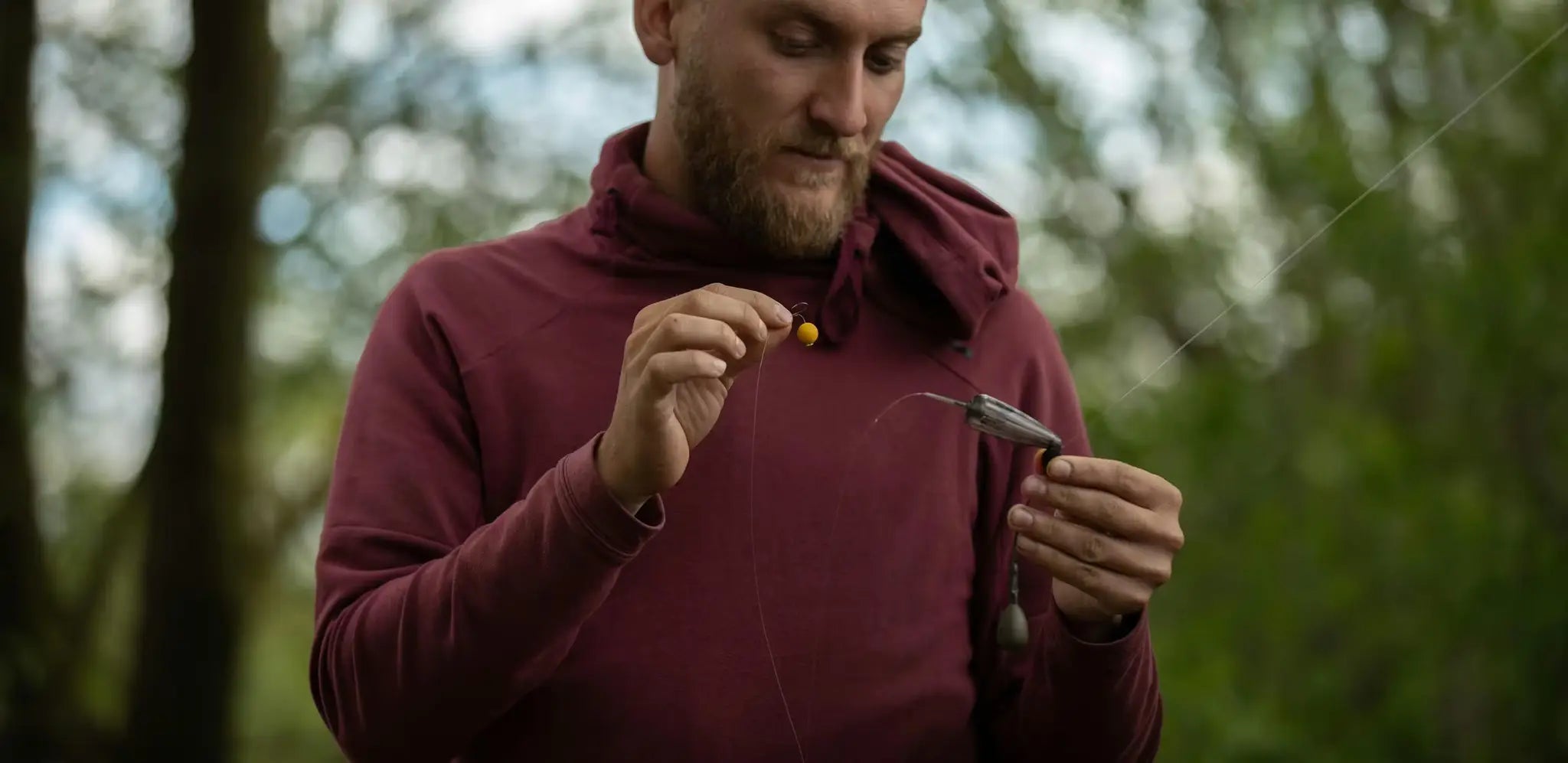 Man in maroon hoodie holds adjustable zig fishing lure with orange bead