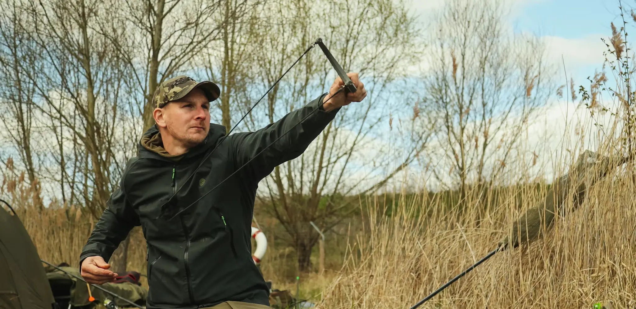Man in camo cap and black jacket holding Katapults bow with dark arrow