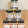 Clear glass flavour pots tutti fruitti with black lids containing golden-yellow liquid flavours developed for bait use
