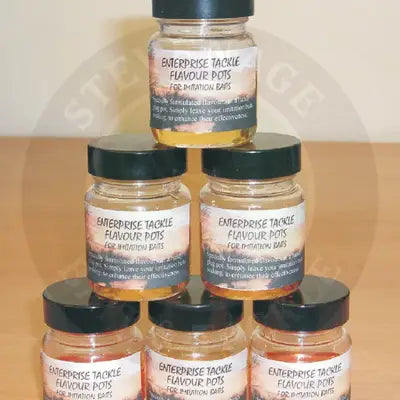 Clear glass flavour pots tutti fruitti with black lids containing golden-yellow liquid flavours developed for bait use