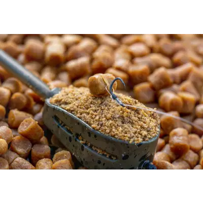 A black speckled fishing bait scoop with brown granular fish food holding a hook line for smwg bait rigs packaging