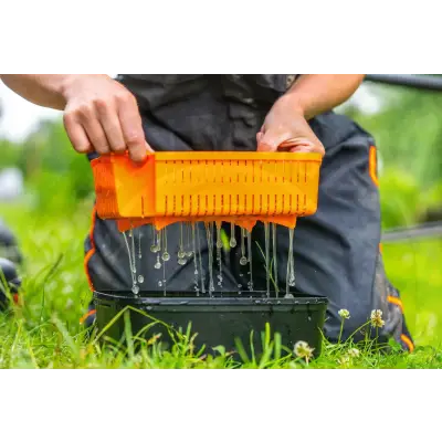 Bright orange plastic guru bait strainer with vertical slits draining into black basin 5 pint bait strainer