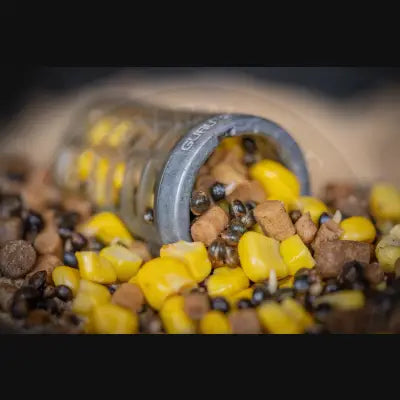 Gray plastic guru bait container spilling yellow corn kernels and brown pellets for loose particles bait use