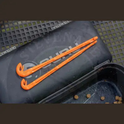 Bright orange plastic fishing rod holders with curved ends resting on a black guru loop tyer case by Tackle Guru