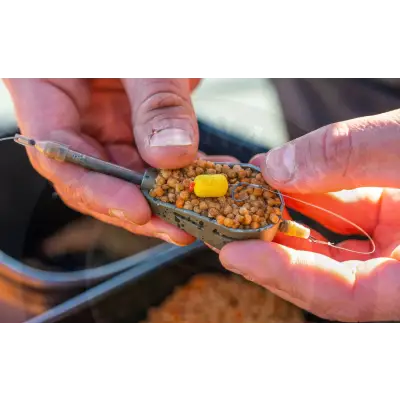 A metallic olive green tackle guru micro hair stops tray filled with brown pellets and a yellow cube attractant for stevenage bait