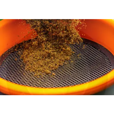 Orange plastic tackle guru multi riddle sieve with metal mesh containing brown granular bait for mainline match 18l