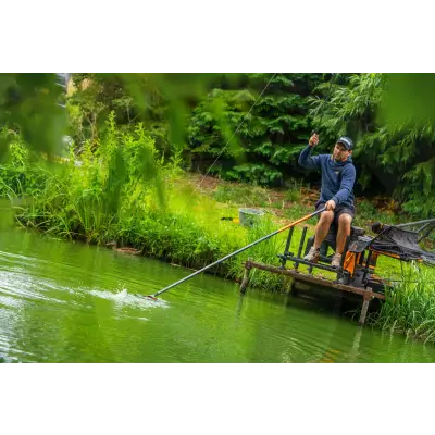 A man in navy blue hoodie uses a black and orange n-gauge pro handle fishing rod on a wooden platform by Tackle Guru