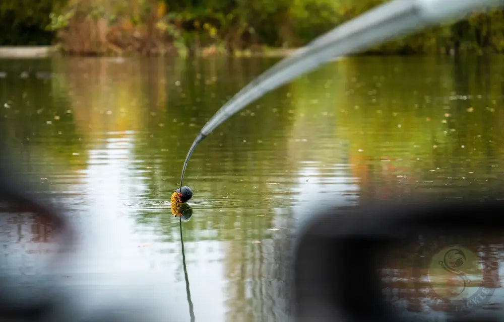 A sleek fishing rod with a black tip and stevenage bait attached used with tackle guru rapid release pole cups