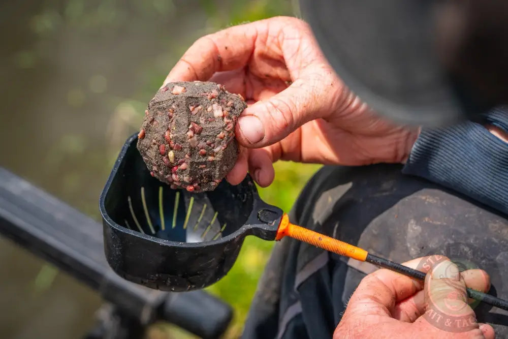 A muddy irregularly shaped stevenage bait ball with red and white pellets in tackle guru rapid release pole cups