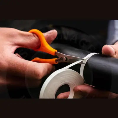 Orange-handled tackle guru serrated rig scissors cutting white adhesive tape from black cylindrical object