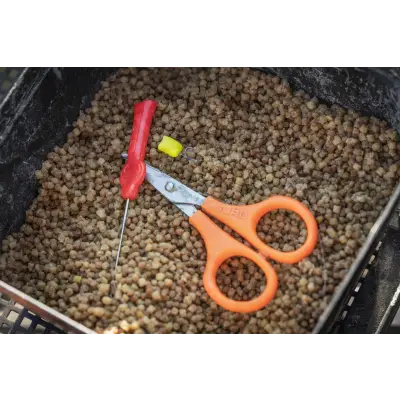 Tackle Guru serrated rig scissors with fluorescent orange handles and silver blade resting on brown pellet bait
