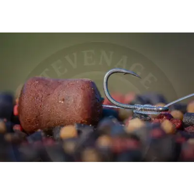 A metallic tackleguru smwg barbed fishing hook with coiled wire wrap next to a brown stevenage bait pellet