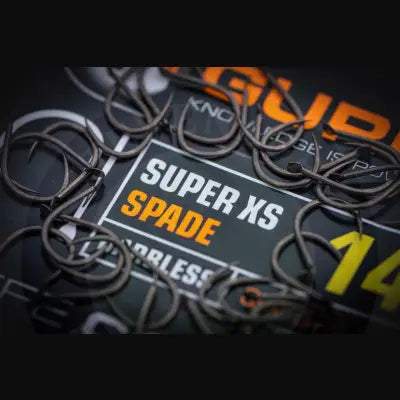 Black metal fishing hooks scattered around a tackle guru super xs spade branded packaging label for stevenage bait