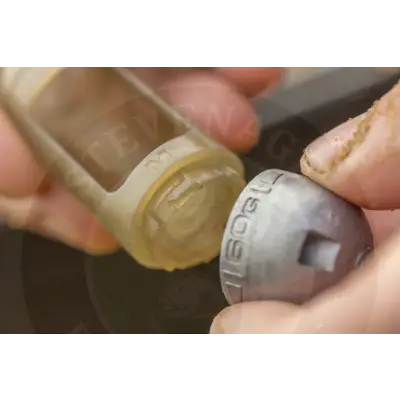 A translucent yellow plastic bottle cap with engraved m and silver screw-on lid on tackle guru small window feeder